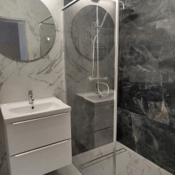 Jarosław Chróściński usługi wykończeniowe - Nowoczesna łazienka z kabiną prysznicową typu walk-in, umywalką z szafką i okrągłym lustrem. Marmurowe płytki w odcieniach szarości i bieli. Minimalistyczny design.