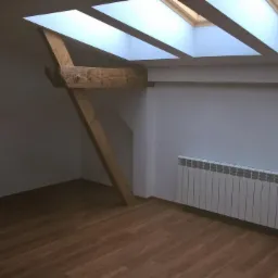 Poddasze po remoncie: drewniana belka konstrukcyjna, okna dachowe w suficie, biały grzejnik na ścianie, panele podłogowe w kolorze drewna.