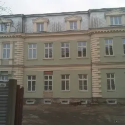 Odnowiona elewacja kamienicy w odcieniach zieleni z białymi oknami i szarym dachem. Widoczne zabezpieczenia budowy.