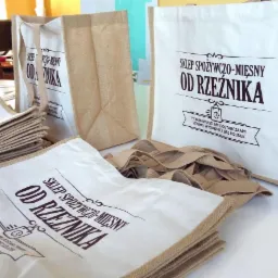 Lniane torby z nadrukowanym logo sklepu spożywczo-mięsnego 'Od Rzeźnika', ułożone na białym stole, widoczne w różnych rozmiarach i ułożeniach.