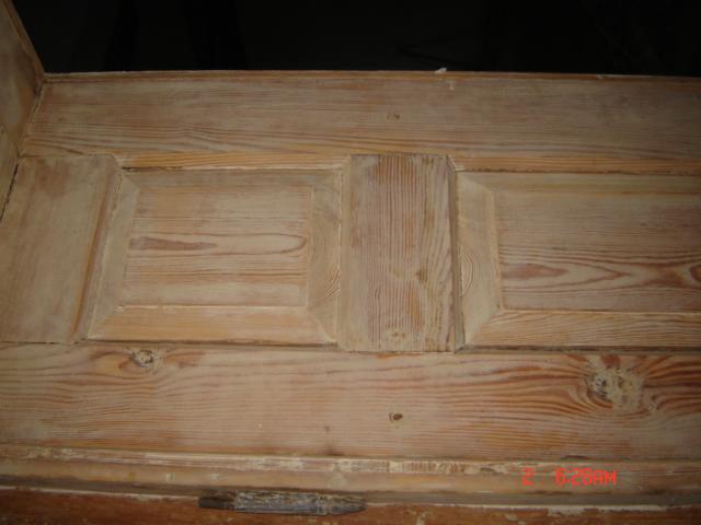 Fragment odnowionej, jasnej, drewnianej boazerii z widocznymi sękami i delikatną strukturą drewna, uchwycony z bliska pod kątem, z widocznym dolnym fragmentem ramy.