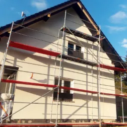 Dom jednorodzinny w trakcie ocieplania elewacji, widoczne rusztowanie i warstwa izolacyjna na fundamencie.