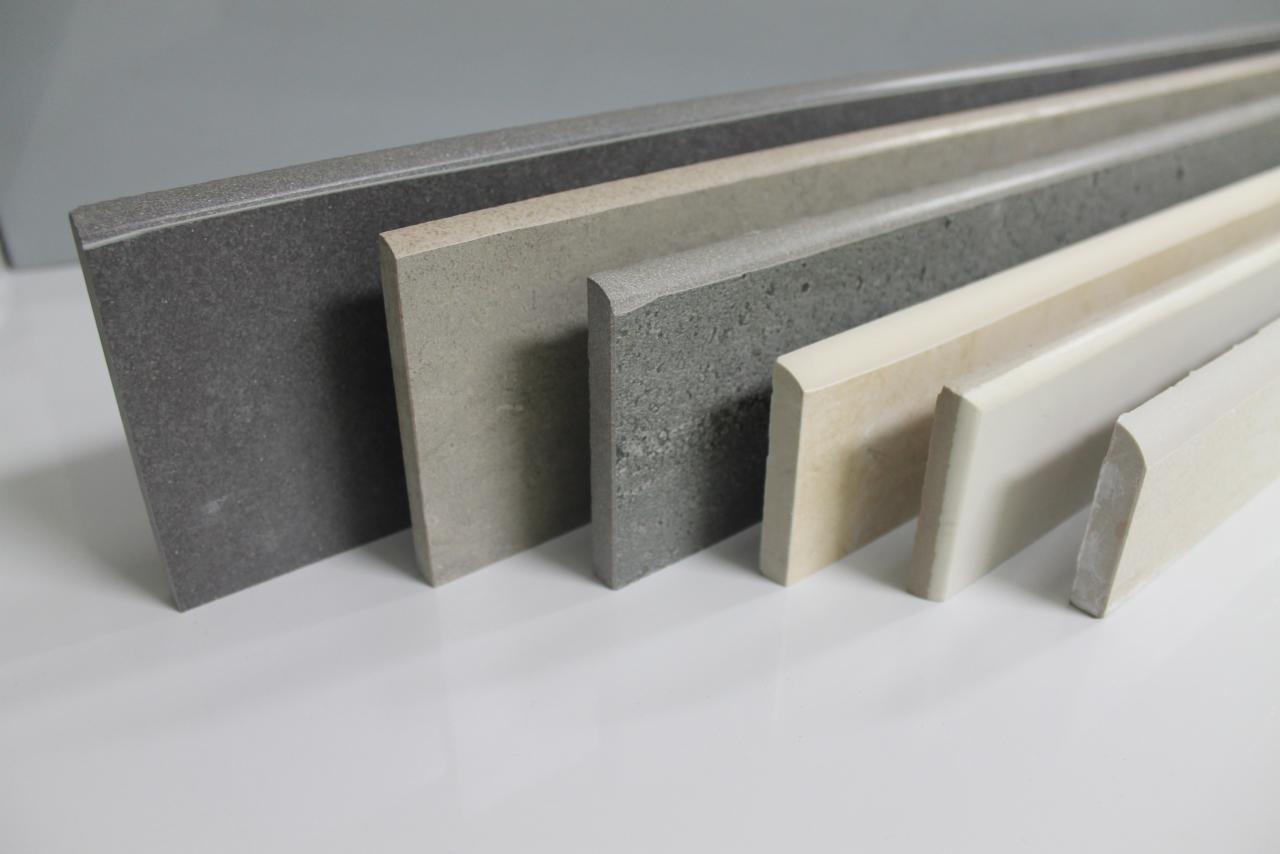 Przekrój poprzeczny listew przypodłogowych z gresu, terakoty i glazury w różnych odcieniach szarości i beżu, z zaokrąglonymi krawędziami, ułożonych rzędem na białym tle.