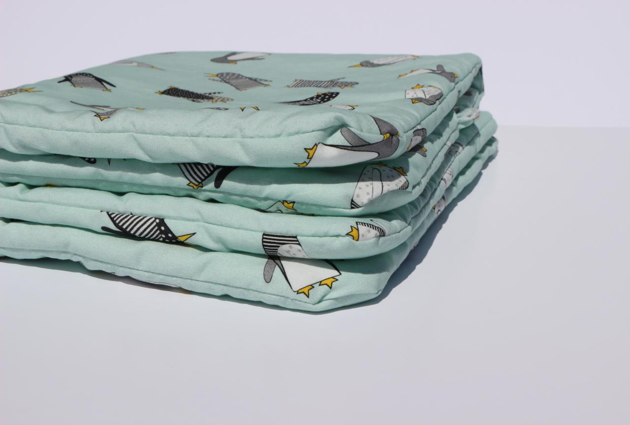 Stos poduszek na krzesła z miętowej tkaniny w pingwiny, uszytych w Szczecinie, z widocznym pikowaniem i żółtymi detalami na wzorze.