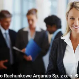 Uśmiechnięta blondynka w marynarce w paski na tle rozmytej grupy osób w biurze.