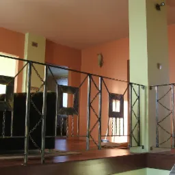Nietypowa balustrada wewnętrzna z metalu, z kwadratowymi elementami dekoracyjnymi i łańcuchami, widok z góry na antresolę w pomarańczowym wnętrzu domu.