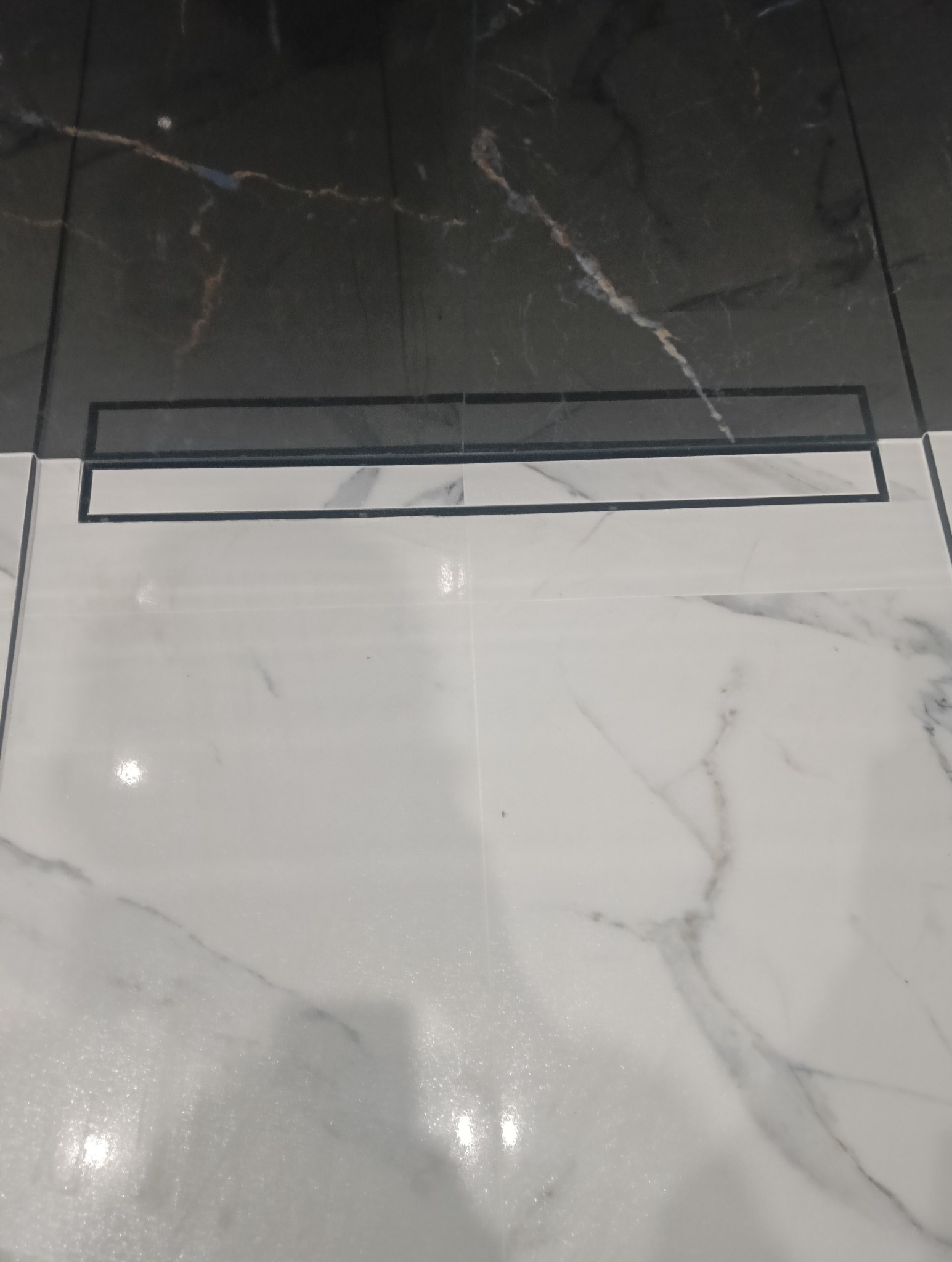 Ułożone płytki podłogowe z odpływem liniowym. Płytki białe i czarne z marmurkowym wzorem.