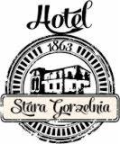 Czarno-białe logo Hotelu Stara Gorzelnia z rokiem 1863 i wizerunkiem budynku w okręgu, stylizowane na retro, z ozdobnymi czcionkami na białym tle.