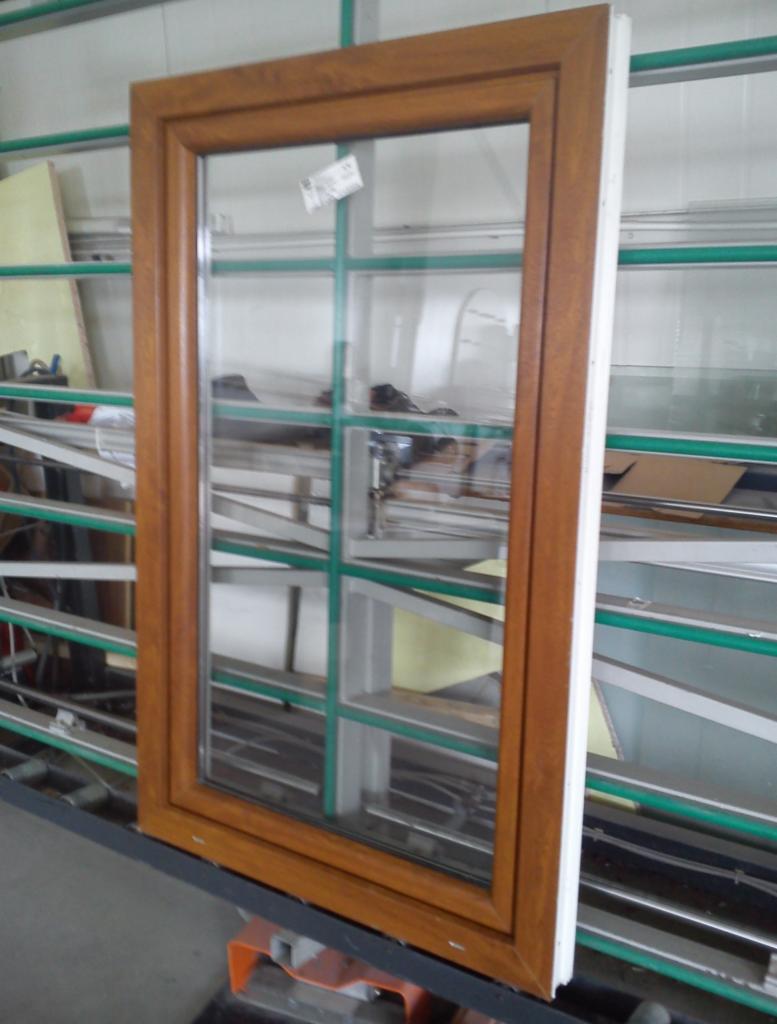 Drewniane okno z szybami zespolonymi, widoczne na tle hali produkcyjnej, z delikatnym odcieniem brązu ramy i białym wykończeniem.