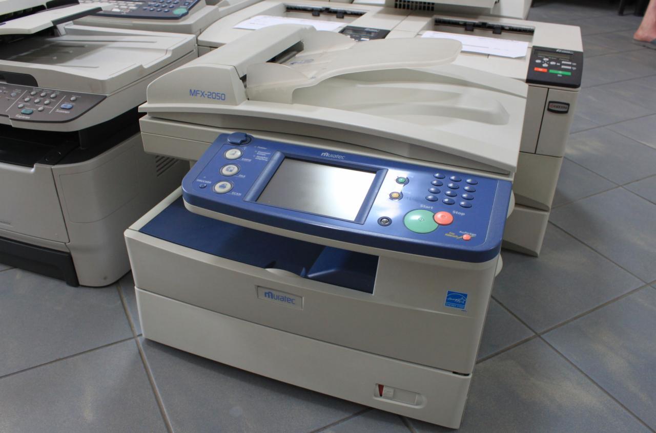 Używana kserokopiarka Muratec z niebieskim panelem sterowania i ekranem dotykowym, widoczna wśród innych urządzeń w magazynie.