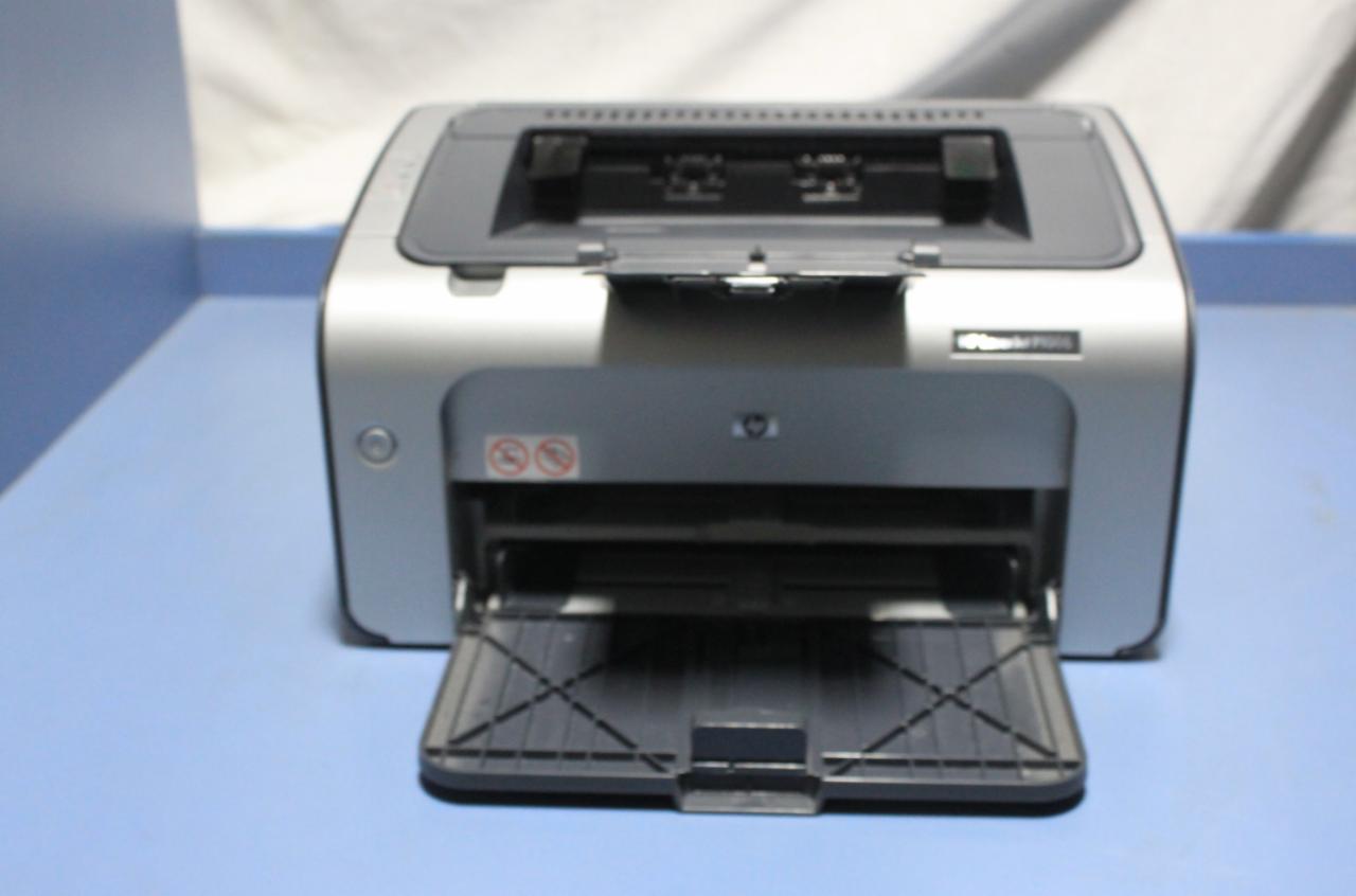 Używana drukarka laserowa HP LaserJet P1005, srebrno-szara obudowa, otwarty podajnik papieru, widoczne symbole ostrzegawcze.