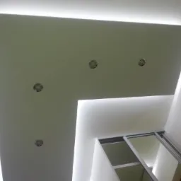 Podwieszany sufit z oświetleniem LED i punktowymi lampami, widok z dołu, fragment szafy wnękowej z przesuwnymi drzwiami, nowoczesne wykończenie wnętrza.