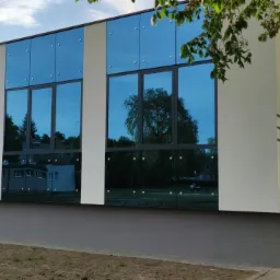 Zmodernizowany budynek Klubu Studenckiego w Słupsku z nową, przeszkloną fasadą, w której odbija się otaczająca zieleń i fragmenty zabudowań osiedla akademickiego.