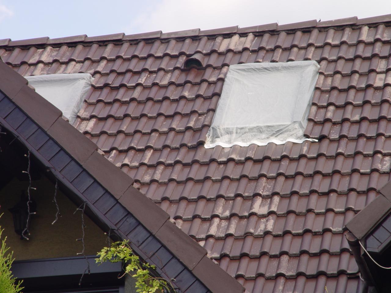 Czerwona dachówka z dwoma oknami dachowymi zabezpieczonymi folią malarską. Widoczne zabrudzenia i mech na powierzchni dachu.