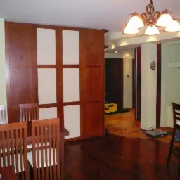 Szafa wnękowa z przesuwnymi drzwiami w odcieniach brązu i beżu, dopasowana do wnętrza z drewnianą podłogą i stołem. Widoczny mężczyzna w tle.