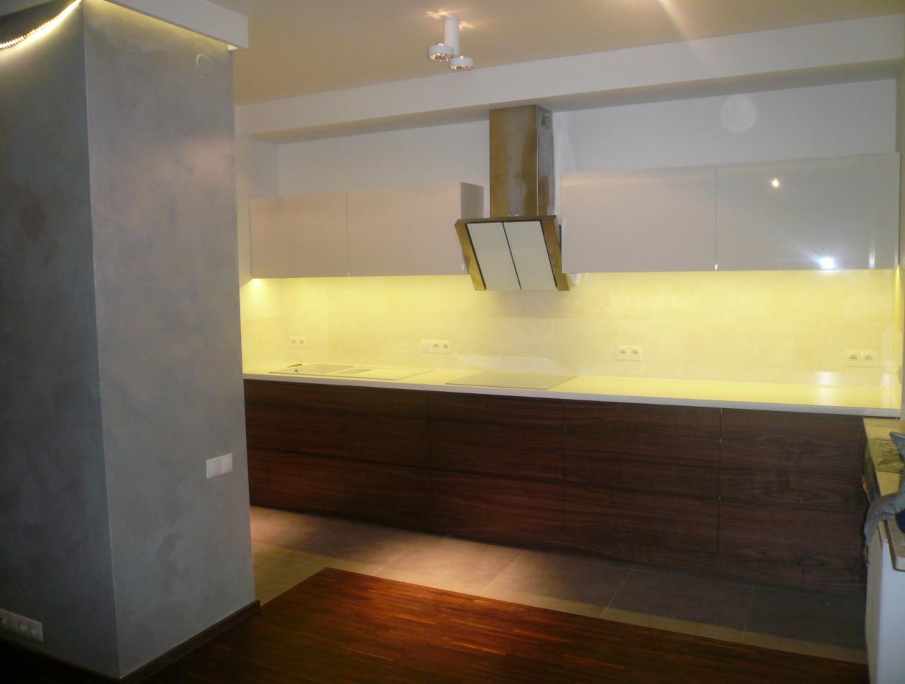 Nowoczesna kuchnia z białymi szafkami górnymi i dolnymi szafkami z ciemnego drewna. Oświetlenie LED pod szafkami.  Minimalistyczny okap.