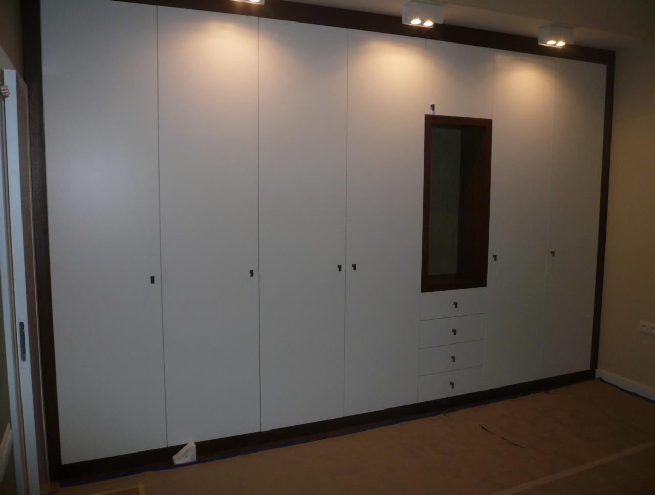 Biała szafa wnękowa z ciemnobrązowymi elementami wykończeniowymi, z lustrem i szufladami, wykonana na wymiar w Podkowie Leśnej.