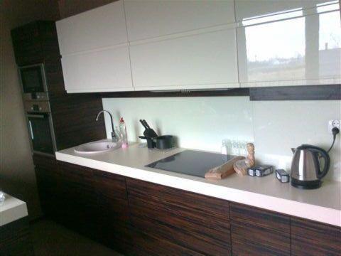 Nowoczesna kuchnia z białymi szafkami górnymi i ciemnymi, drewnopodobnymi szafkami dolnymi. Widoczny zlew, płyta indukcyjna i czajnik elektryczny.