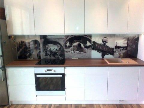 Biała zabudowa kuchenna z drewnianym blatem i czarno-białym panelem szklanym z motywem Paryża. Nowoczesny design, proste fronty, widoczny piekarnik i zlew.