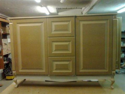 Beżowa szafka łazienkowa z trzema szufladami i dwojgiem drzwiczek, na ozdobnych nóżkach, w trakcie produkcji, w warsztacie.