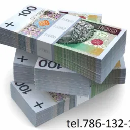 Stosy spiętych banknotów 100 zł w białych banderolach z nadrukowaną wartością 10000 zł, ułożone na sobie, widoczny numer telefonu na dole zdjęcia.