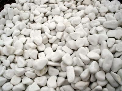 Białe, gładkie otoczaki marmurowe, ułożone w dużym skupisku. Kamienie o różnych kształtach i rozmiarach, z delikatnymi cieniami podkreślającymi ich fakturę.