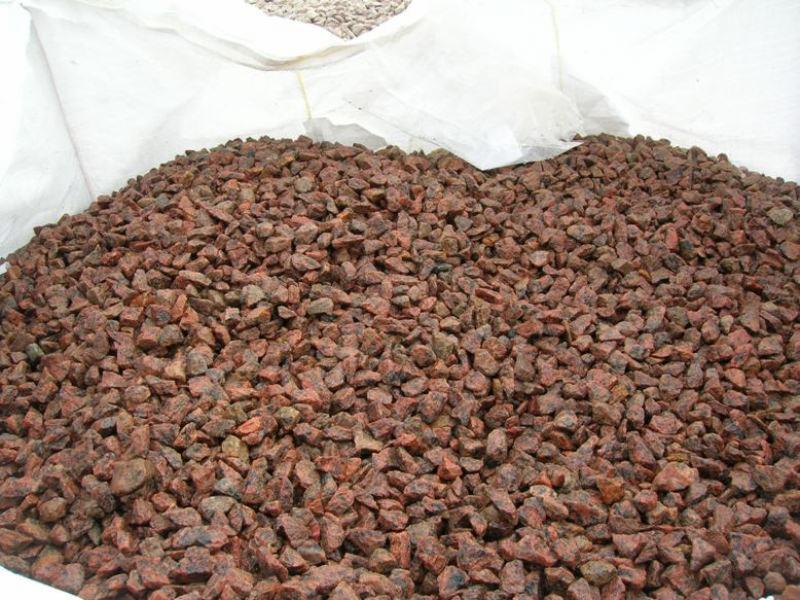 Kopalniana sterta czerwono-brązowego grysu granitowego w worku typu big bag, drobne kamienie dekoracyjne do ogrodu, zarys worka widoczny w tle.