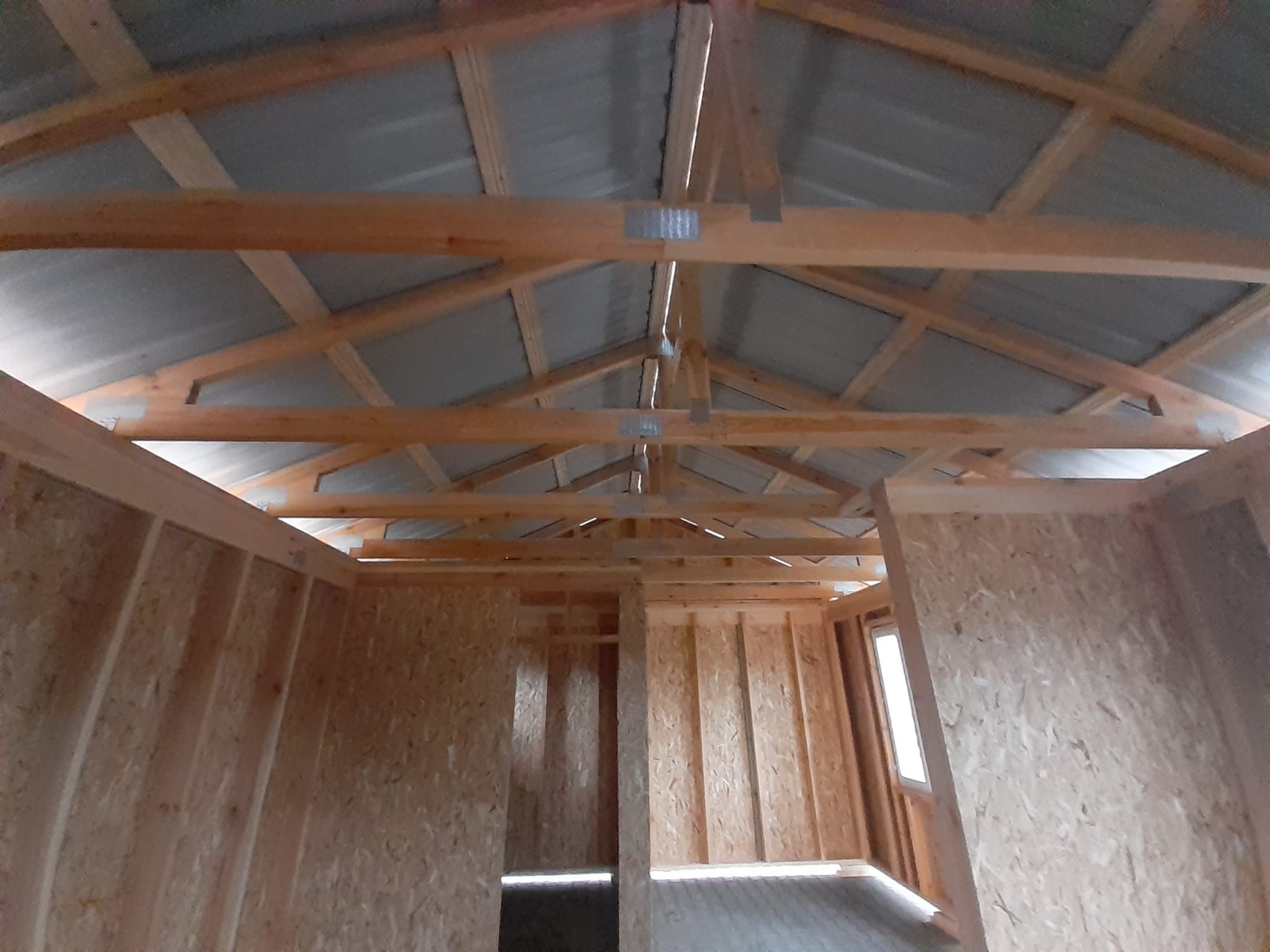 Wnętrze domu szkieletowego w trakcie budowy, widoczne drewniane ściany z płyty OSB, konstrukcja dachu z metalowym pokryciem, okno w ścianie bocznej.