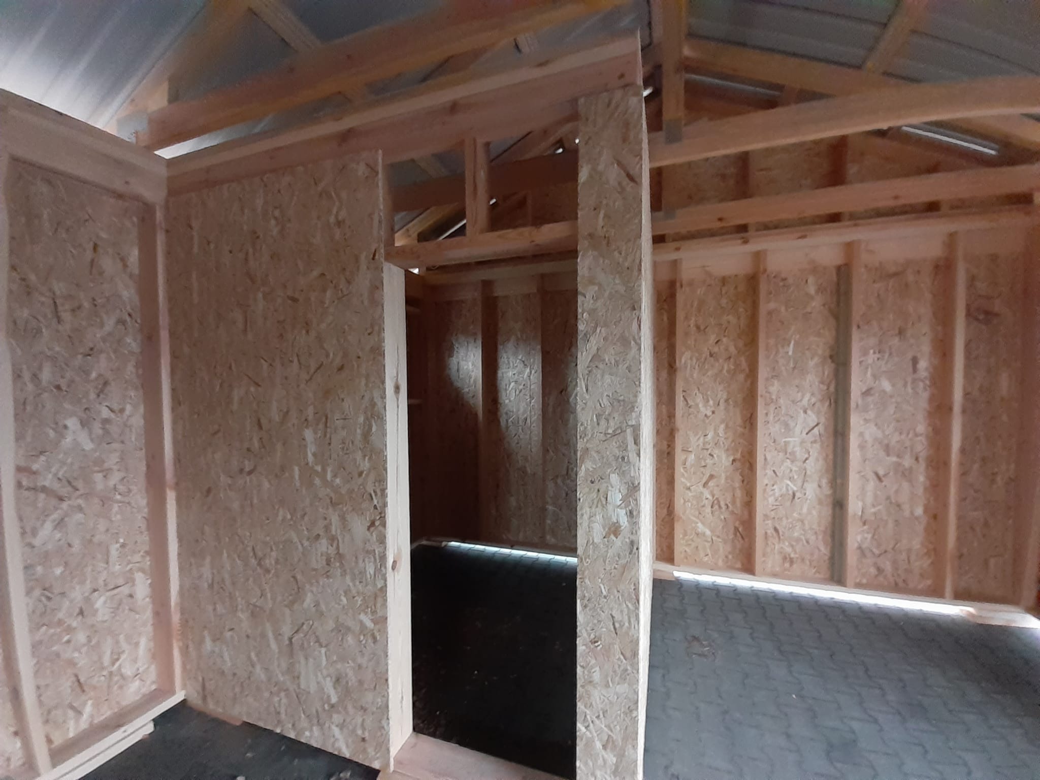 Wnętrze konstrukcji z drewnianych belek i płyt OSB, w trakcie budowy, widoczny zarys pomieszczenia z podłogą wyłożoną kostką brukową.