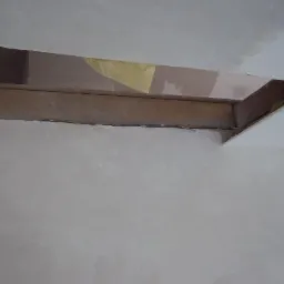 Fragment ściany i sufitu po tynkowaniu, widoczny drewniany element konstrukcyjny w otworze. Świeże, jasne tynki. Detal wykończenia wnętrza w trakcie prac.