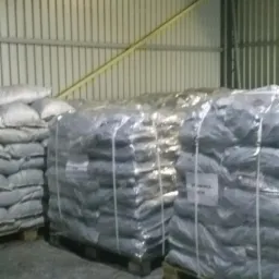 Magazyn z zapasem worków na paletach, owiniętych folią, wewnątrz metalowej hali. Widoczne etykiety na workach.