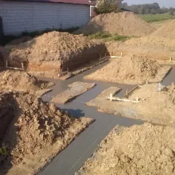 Wylane fundamenty pod budynek z widocznymi wykopami, deskowaniem i hałdami ziemi w słoneczny dzień.