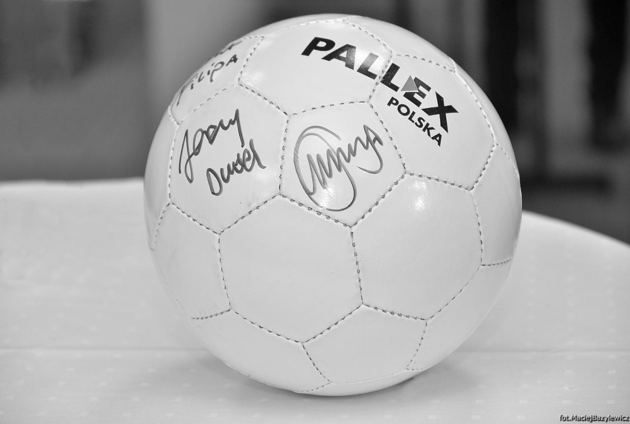 Biała piłka z logo Pallex Polska i autografami, leżąca na białym obrusie, zdjęcie czarno-białe.