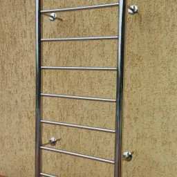 Metalowa drabinka z poziomymi szczeblami przymocowana do ściany o chropowatej fakturze, wsparta na drewnianej belce.