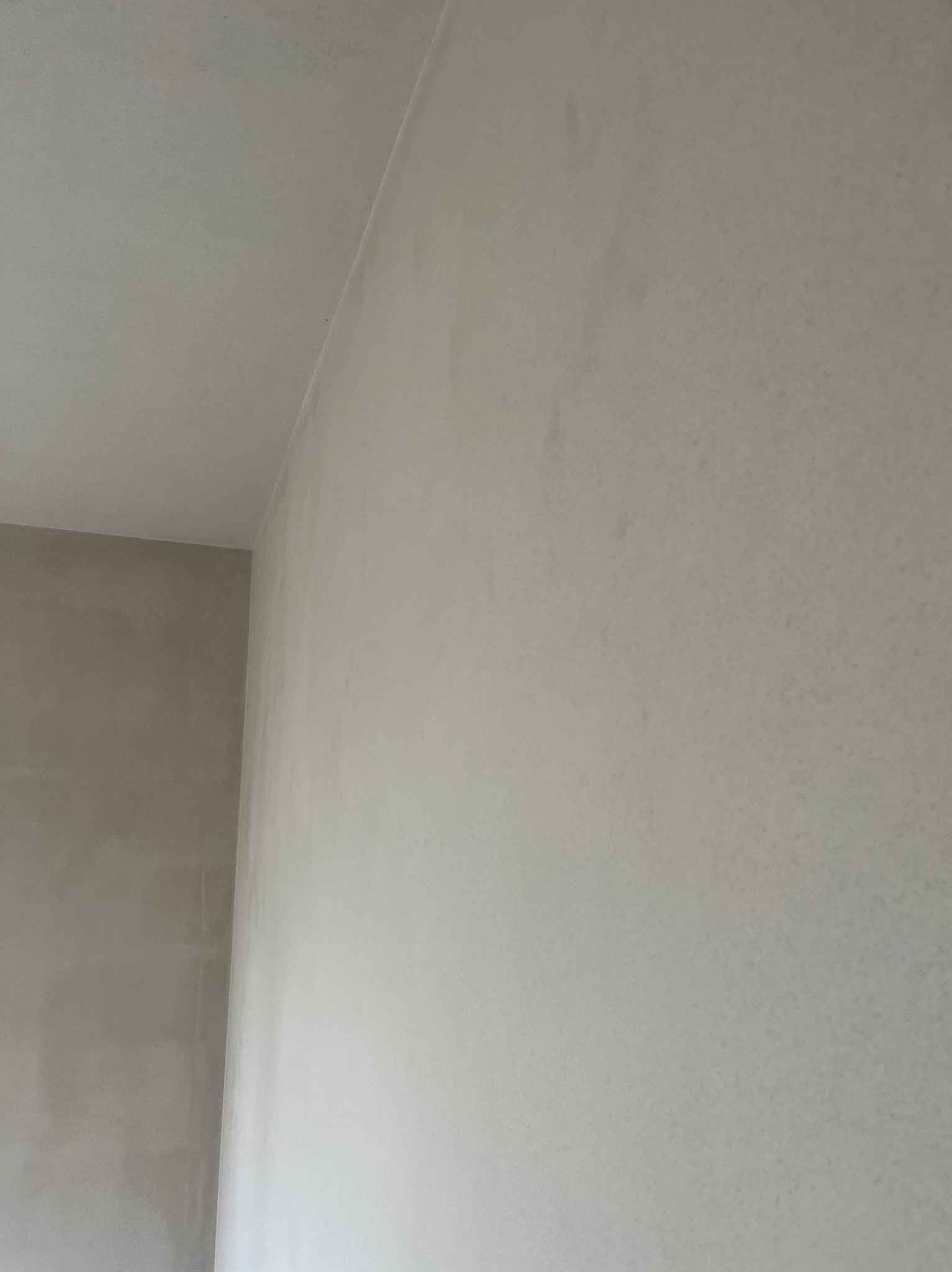 Fragment ściany i sufitu po nałożeniu gładzi, widoczne niedoskonałości wymagające szlifowania przed malowaniem, szara kolorystyka.