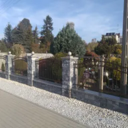 Nowoczesne ogrodzenie z szarej kostki i metalowymi przęsłami na tle zadbanego ogrodu z domem w oddali.