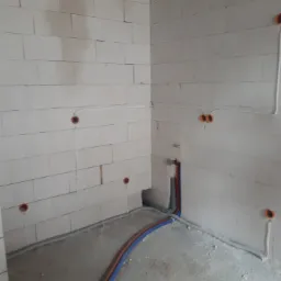 Surowy stan instalacji elektrycznej i wodnej w nowym budynku: widoczne przewody elektryczne w peszlach oraz rury wodne w ścianach z betonu komórkowego.