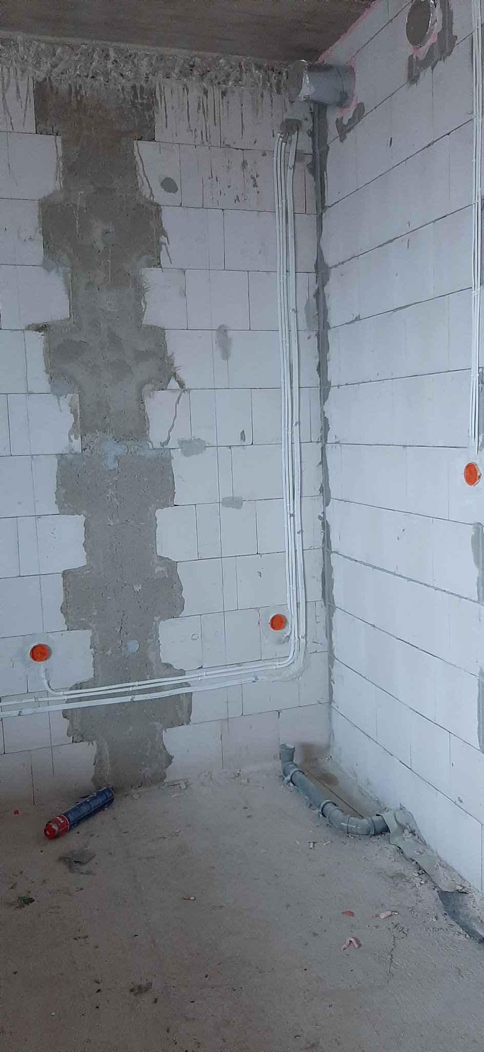 Wnętrze w trakcie remontu: białe ściany z betonu komórkowego, częściowo pokryte tynkiem, z widocznymi przewodami elektrycznymi w białych rurkach PCV oraz puszkami instalacyjnymi. Na podłodze leżą...