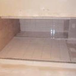 Flizzz Usługi Remontowo-Wykończeniowe - Wnęka wyłożona jasnymi, kwadratowymi płytkami ceramicznymi. Widoczne świeże fugi i delikatne odbicia światła na powierzchni płytek. Minimalistyczne wykończenie.