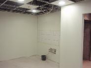 Wnętrze biura w trakcie prac wykończeniowych: pomalowane ściany w jasnym odcieniu, sufit podwieszany z widoczną instalacją, przygotowane punkty instalacyjne na ścianie.