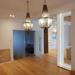 Dwa dekoracyjne żyrandole łańcuchowe oświetlające wnętrze domu w Międzychodzie, z podświetlanym LED-ami elementem architektonicznym i parkietem w trakcie układania.