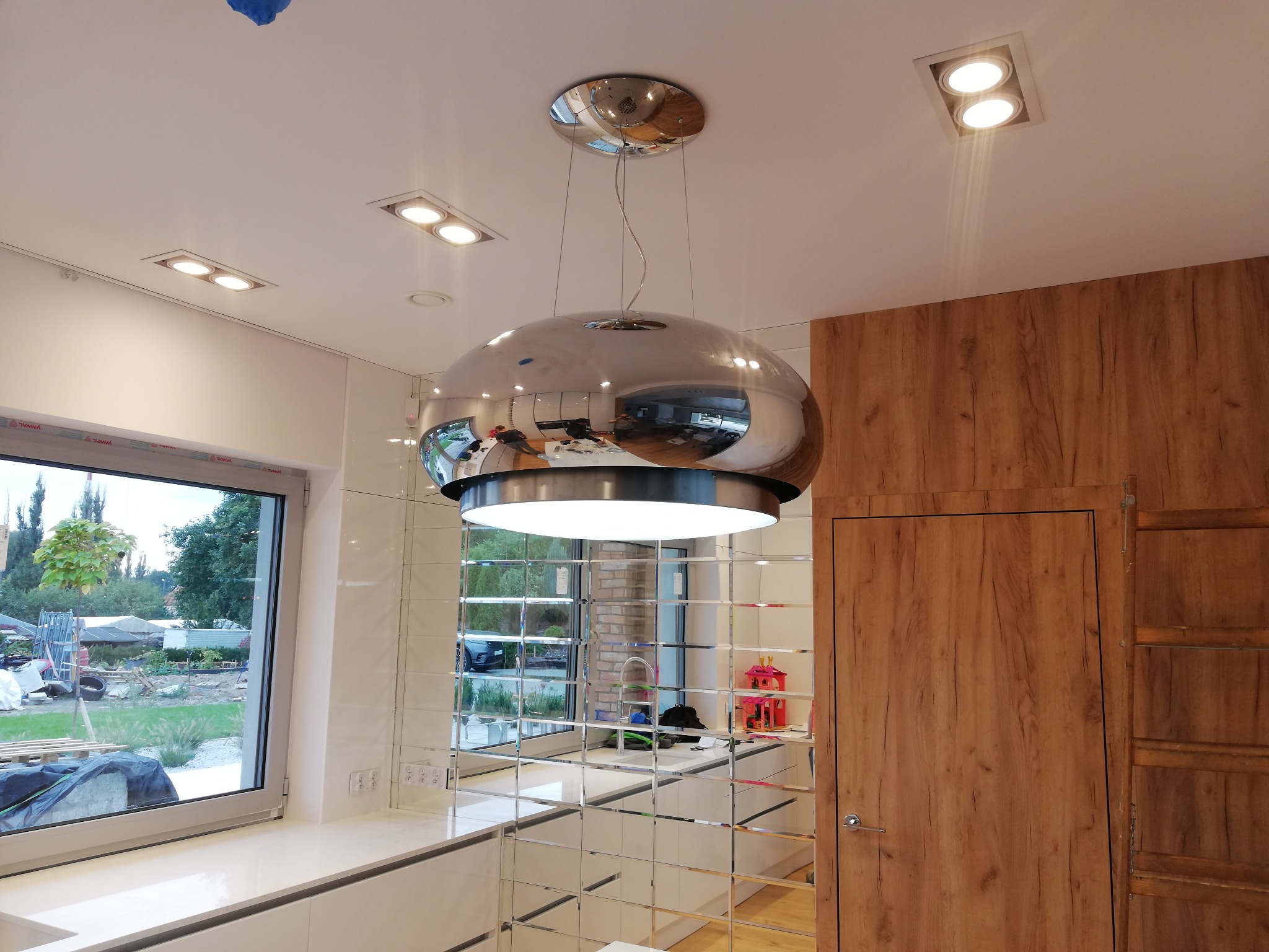 Nowoczesna kuchnia z lustrzaną ścianą, okrągłym chromowanym okapem i wbudowanymi lampami sufitowymi