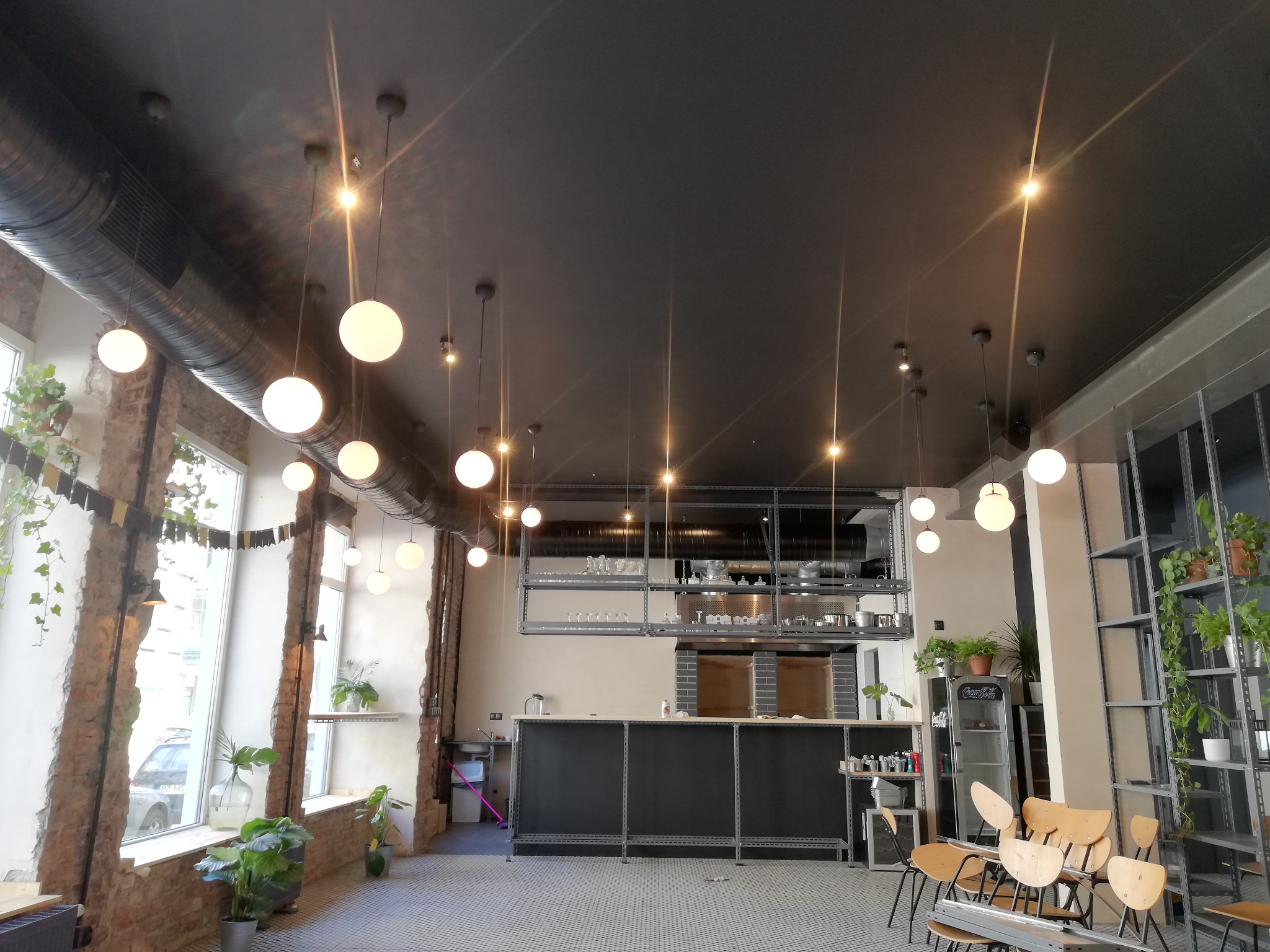 Wnętrze lokalu gastronomicznego z widocznym systemem wentylacji pod sufitem i kulistymi lampami wiszącymi.