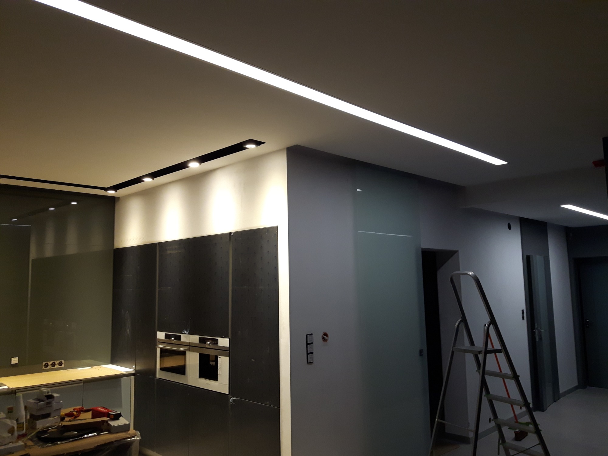 Nowoczesna kuchnia z zamontowanym oświetleniem LED liniowym i punktowym, widoczna drabina malarska.