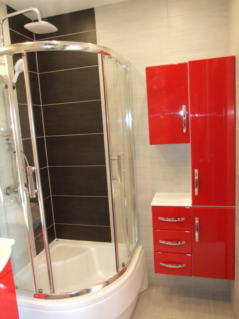 Nowoczesna kabina prysznicowa z czarnymi płytkami i czerwonymi szafkami łazienkowymi. Ujęcie prezentuje wykończoną łazienkę z dbałością o detale.