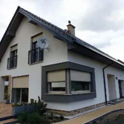 Nowoczesny dom jednorodzinny z szarą stolarką okienną i drewnianym tarasem, widok z ogrodu w pochmurny dzień.