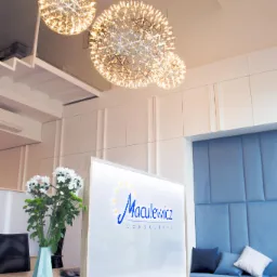 Recepcja biura z logo Maculewicz Consulting, kwiatami w wazonie i dekoracyjnymi lampami kulistymi.