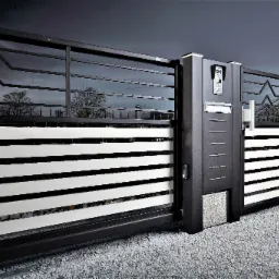 Nowoczesna, przesuwna brama wjazdowa z metalowymi przęsłami, białymi poziomymi panelami i domofonem, na tle szarego nieba i oświetlenia ulicznego.