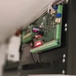 Zamontowana płyta główna alarmu w czarnej obudowie, widoczne diody LED i przewody podłączone do złączek.