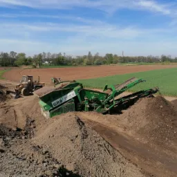 Praca przesiewacza do ziemi z koparką w tle na tle pola i drzew, błękitne niebo
